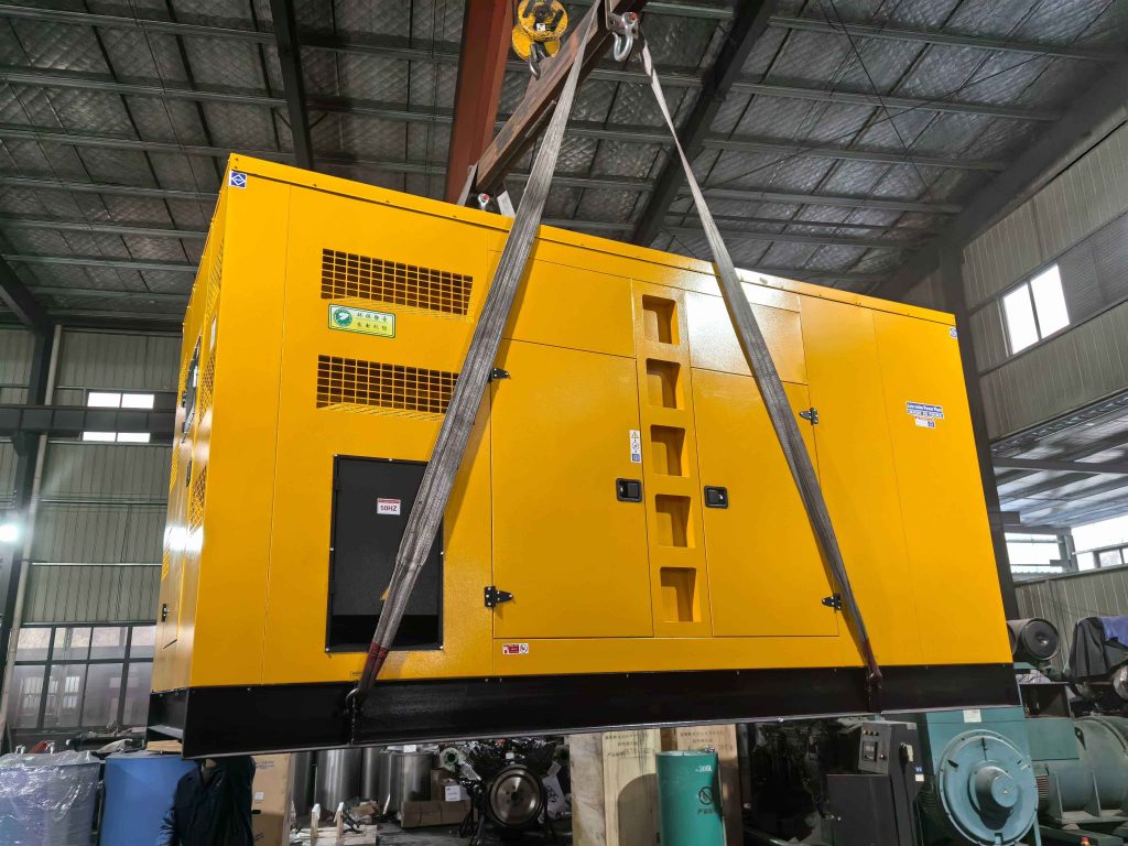 Yellow containerised generator set lifted by crane slings inside a workshop before dispatch to an export site